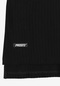 Czarna prążkowana tkanina o teksturowanej powierzchni. Widoczna metka z napisem „PROSTO” w białym kolorze na czarnym tle. Obrębione krawędzie.
