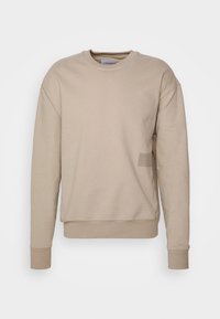 Beige sweatshirt met een ronde halslijn, lange mouwen en geribbelde manchetten. Voorzien van een subtiele logopatch op de voorkant linksonder. Gladde textuur.