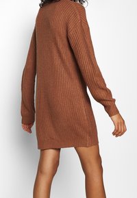 Strickkleid in verbranntem Orange, mit lockerer Passform, langen Ärmeln, gerippter Textur und einem leicht verlängerten hinteren Saum.