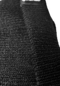 Black textured fabric with a ribbed pattern, showcasing a soft, woven appearance. Features a visible brand label at the top edge.
