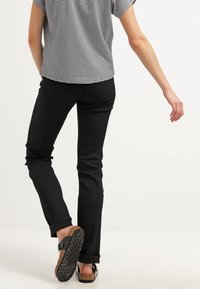 Jeans neri a vestibilità slim, abbinati a una maglietta a maniche corte a righe. Sandali neri con suola strutturata e cinturino regolabile.
