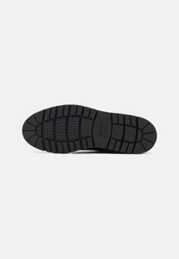 Suela de zapato de goma negra con un patrón texturizado, que presenta surcos profundos y perforaciones para un mejor agarre y flexibilidad. Marca Geox visible.
