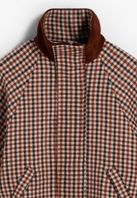 Chaqueta de lana con estampado de pata de gallo en tonos óxido y marrón, que cuenta con un alto cuello de pana y bolsillos frontales.