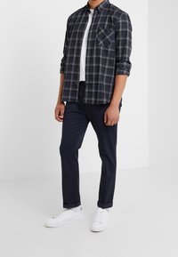 Blå rutigt skjorta med knappar och lång ärm, vit T-shirt med rund hals, marinblå byxor och vita sneakers. Har en bröstficka.