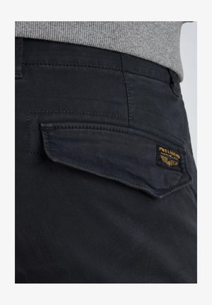 Pantaloni scuri in cotone con una finitura testurizzata. Presentano una tasca a svolazzo con un patch logo giallo e nero.