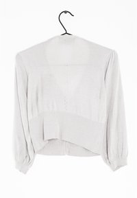 Ljusgrå, stickad kort cardigan med puffärmar och ribbat avslut. Har ett strukturerat mönster och en oregelbunden nederkant.