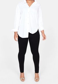 Vit skjorta med krage och långa ärmar, i kombination med svarta leggings. Skjortan har en rundad nederkant och en avslappnad passform.