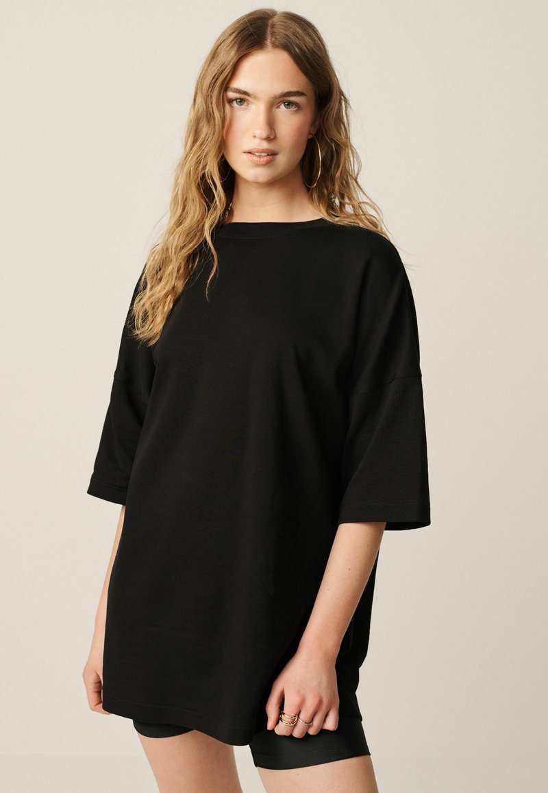 Zwarte oversized t-shirt met korte mouwen, gemaakt van zachte stof. Heeft een ronde halslijn en een relaxed fit, gedragen over zwarte fietsbroeken.