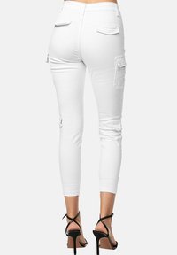 Witte cargobroek met achterzakken, beschadigde details en een strakke pasvorm. Gecombineerd met zwarte hoge sandalen, die een slanke silhouette laten zien.