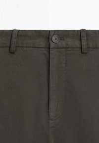 Close-up of dark brown trousers showing button closure, belt loops, and fabric texture.