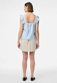 Top azzurro chiaro senza maniche con spalline arricciate, schiena bassa e dettaglio arricciato; abbinato a una gonna beige e scarpe nere.