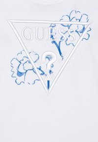 Bijela pamučna majica s plavim izvezenim trokutastim logotipom s natpisom "GUESS®", floralnim dizajnom, upitnikom i natpisom "WASTED JEANS".