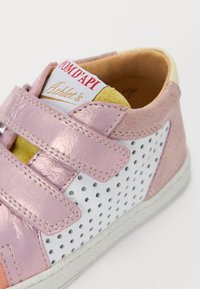 Sneaker in pelle rosa con pannelli perforati bianchi, cinturini in Velcro e interno color beige. Presenta un logo dorato sulla linguetta.