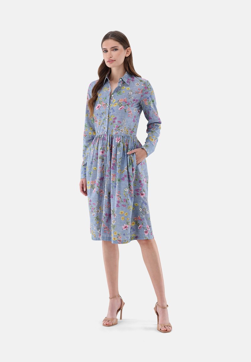 Abito a camicia in tessuto azzurro chiaro con motivi floreali rosa e gialli. Presenta maniche lunghe, una vita arricciata e tasche laterali.