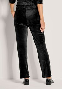 Schwarze Samt-Hosen mit geradem Bein, glatter Textur und elastischem Bund, kombiniert mit glänzenden schwarzen Schuhen. Rückansicht gezeigt.