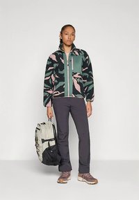 Fleecová bunda v černé barvě s růžovými a zelenými listovými vzory, přední zip, náprsní kapsa; doplněná tmavými kalhotami a šedým batohem.