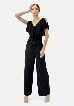 Combinaison noire avec un décolleté en V et des épaules froncées. Présente une taille ceinturée, des jambes larges plissées et une texture lisse.