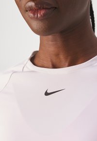 T-shirt en blanc évacuant l'humidité de Nike avec un logo noir. Il présente un col rond et une texture lisse. Gros plan sur la zone du cou et de l'épaule.