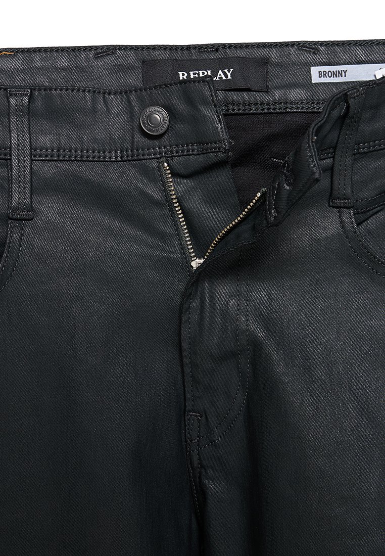 Czarne dżinsy denimowe z otwartym zamkiem błyskawicznym i guzikiem, markowane jako Replay, z metką, na której w środku pasa widnieje napis "Bronny".