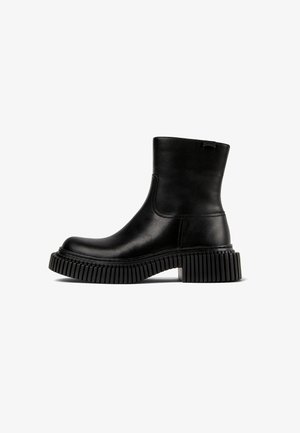 Black leather ankle boot with a rounded toe, elastic side panels, and a thick, ridged rubber sole. Minimalist design with subtle branding.