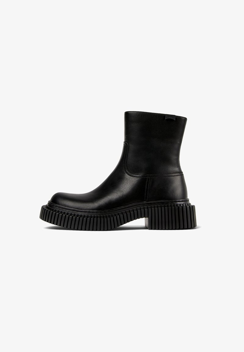 Stivale alla caviglia in pelle nera con punta arrotondata, pannelli laterali elasticizzati e suola in gomma spessa e rigata. Design minimalista con branding discreto.
