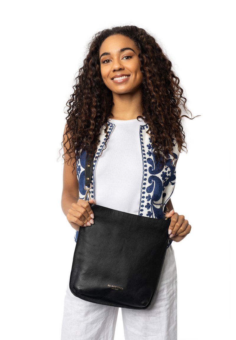 Bolso de hombro de cuero negro con herrajes dorados. Presenta una textura suave, forma rectangular y un diseño minimalista.