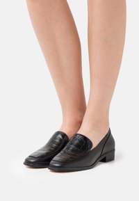 Musta nahkakengät, joissa on teksturoitu krokotiiliaineisesta nahasta valmistettu etuosa, matala lohkarekenkäkorko ja sileät sivupaneelit. Klassinen liukuva malli.