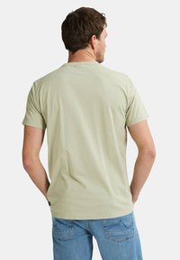 Hellgrünes T-Shirt mit kurzen Ärmeln und Rundhalsausschnitt, aus glattem Stoff und mit lockerer Passform, kombiniert mit blauen Jeans.