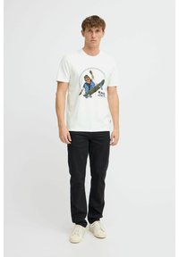 Hvid bomulds T-shirt med et farverigt grafisk tryk af en skateboarder med teksten "ROLL WITH IT". Kombineret med sorte jeans og cremede sneakers.