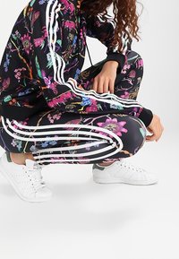 Blommigt svart träningsset med vita ränder, med livfulla färger och mönster. Utrustad med en fitted design och matchande vita sneakers.