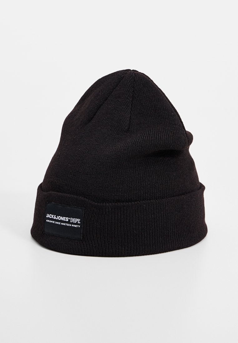 Zwarte gebreide beanie met een opgerolde rand, voorzien van een rechthoekig zwart label met witte tekst. Zachte textuur met een klassieke vorm.