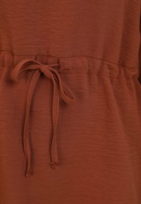 Brown fabric with a textured finish; features a drawstring waist tie and elastic at the top for adjustable fit.