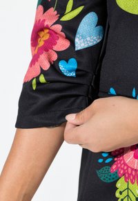 Schwarzes Blumenkleid mit lebhaften rosa und blauen Blumen sowie grünen Blättern. Glattes Material und geraffte Ärmeldetails.