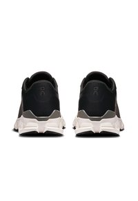 Des chaussures de course noires avec une tige en mesh texturé, des accents gris au niveau du talon et une semelle intermédiaire blanche. Le design présente un talon arrondi et des détails de logo.