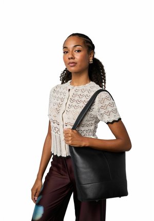 Černá kožená taška přes rameno s hladkou texturou, obdélníkového tvaru a minimálním kováním. Nosená na rameni, doplněná krémovým pleteným topem a tmavými kalhotami.