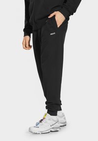 Czarne dresowe spodnie o gładkiej fakturze i elastycznych mankietach, z bocznymi kieszeniami i małym białym logo na lewym biodrze.