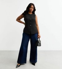 T-shirt sans manches noir avec un devant boutonné et deux poches, associé à un jean bleu à jambe large et des talons aiguilles noirs, tenant un petit sac à main noir.