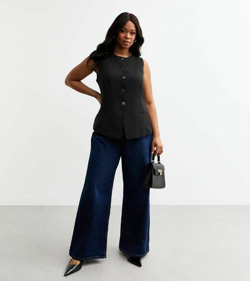 T-shirt sans manches noir avec un devant boutonné et deux poches, associé à un jean bleu à jambe large et des talons aiguilles noirs, tenant un petit sac à main noir.