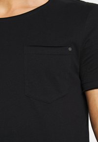 Black short-sleeve shirt with a round neckline and a chest pocket featuring a small metal button on the upper right corner.