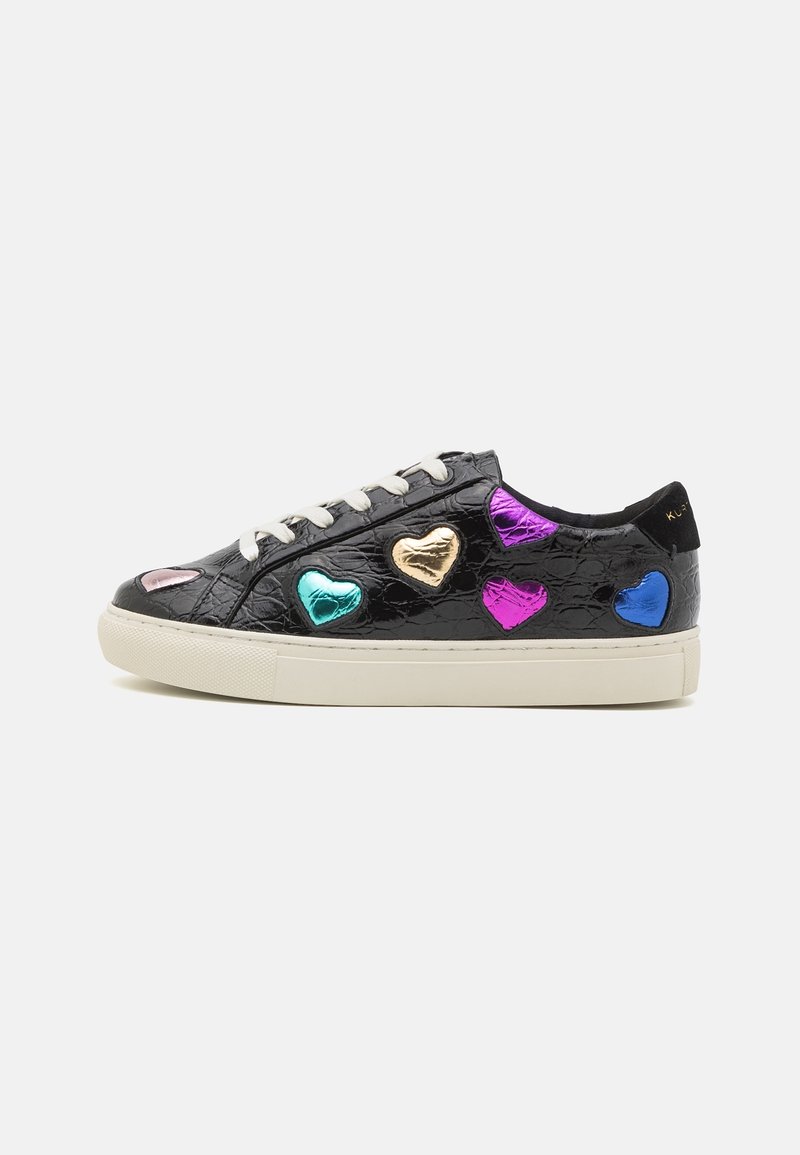 Baskets basses noires avec lacets blancs, semelle beige et patchs en forme de cœur multicolores brillants sur une surface en cuir texturé.