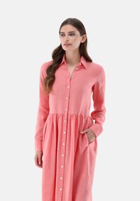 Korallenfarbenes Langarmkleid aus Leinen, mit einer Knopfleiste, gerafftem Bund und seitlichen Taschen. Sanfte Textur mit lässiger Passform.