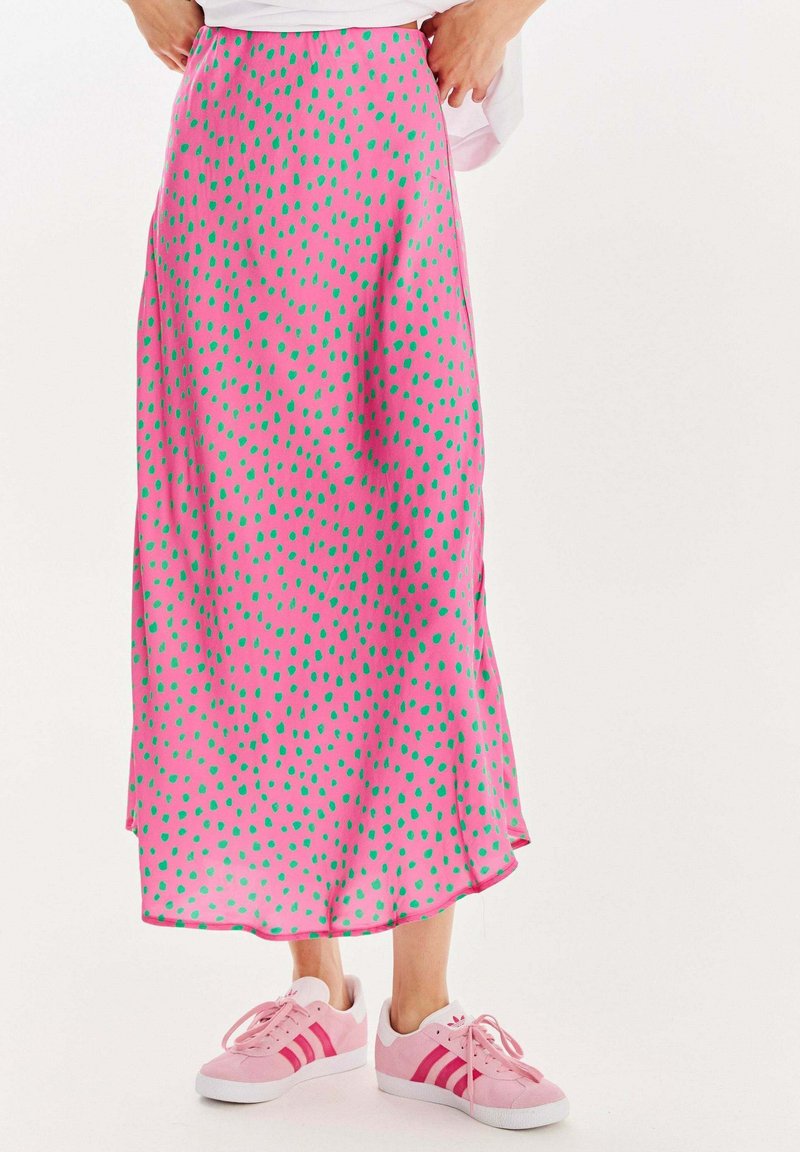 Růžová saténová sukně s zelenými puntíky, střední délky, s bočním rozparkem. Spárována se světle růžovými teniskami. Hladká textura.