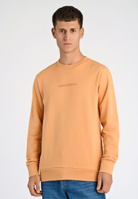 Ljust orange sweatshirt med rund halsringning, ribbad mudd och en subtil präglad logotyp på bröstet. Tillverkad av mjukt, texturerat tyg.
