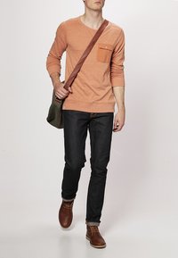 Orange långärmad skjorta med bröstficka, mörka jeans och bruna skor; man som bär en olivgrön budväska.