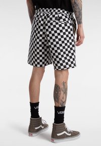 Black and white checkered shorts with an elastic waistband and two back pockets, paired with gray high-top sneakers and black branded socks.