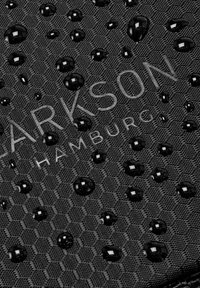 Schwarzer Strukturstoff mit hexagonalem Muster, auf dessen Oberfläche sich mehrere glänzende Wassertropfen befinden. "PARKSON HAMBURG" in hell geprägt.