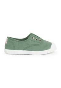 Chaussure slip-on en toile verte avec semelle en caoutchouc blanc et embout. Dispose de deux œillets en métal sur le côté pour la respirabilité.