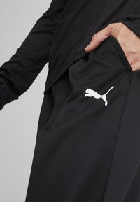 Sorte atletiske bukser med en glat tekstur, prydet med et hvidt Puma-logo på låret og detalje med sidelommer. Letvægtsmateriale.