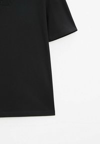 T-shirt noir à manches courtes avec un ourlet droit sur fond blanc, montrant uniquement le côté droit et la manche.
