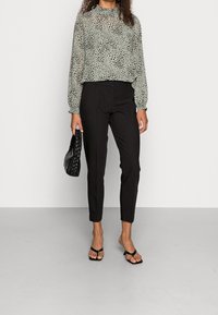 Czarne dopasowane spodnie zestawione z przezroczystą, jasnozieloną bluzką w czarne plamki. Dodatki to pleciona czarna torebka i klapki.